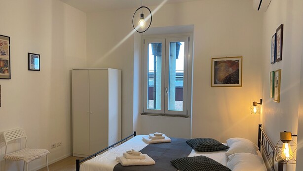 Een slaapkamer met een bed, een kledingkast, een stoel, een raam en een wandlamp.