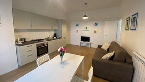 Een moderne keuken met witte kasten, een eettafel met stoelen, een bruine bank en een televisie in de woonkamer.