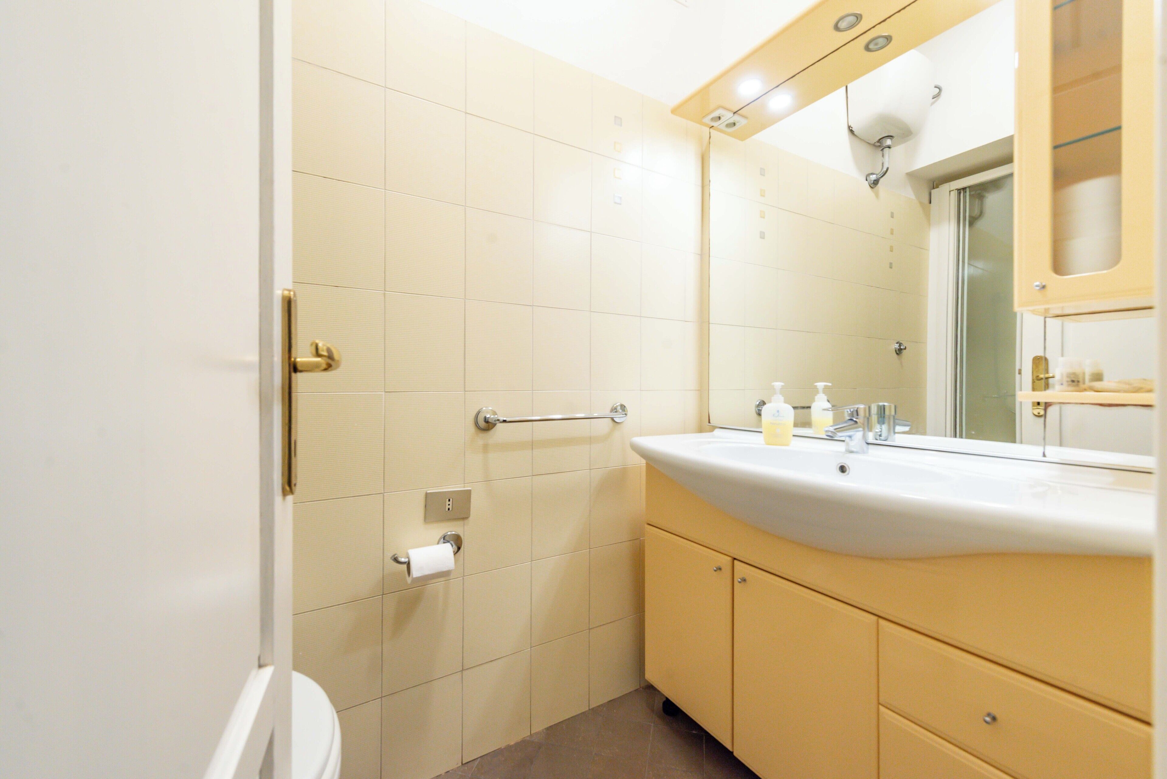 A bathroom with a toilet, sink, mirror, and towel rack.