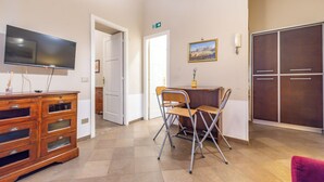 Ein Zimmer mit Flachbildfernseher, einem Holzkasten, klappstühlen, einem Tisch und einem Kleiderschrank.
