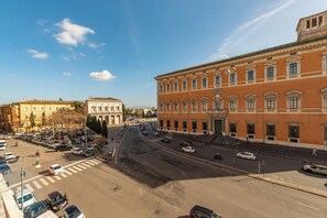 Uma rua larga com edifícios em ambos os lados, incluindo um edifício vermelho imponente com arquitetura clássica.