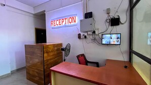 Un área de recepción con un escritorio de madera, una silla roja, un cartel de recepción y una cámara de seguridad instalada.