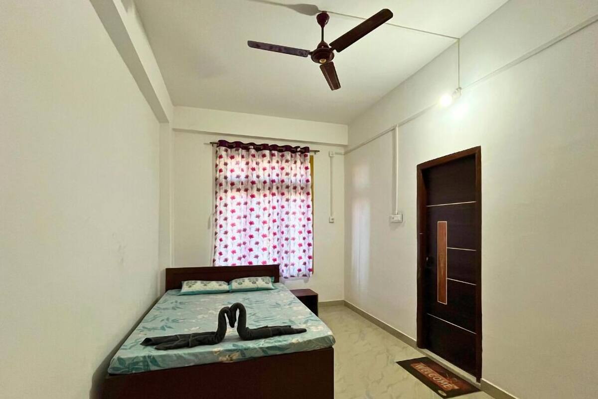 A bedroom with a bed, a ceiling fan, a door, and a window with curtains.