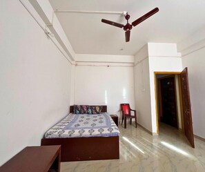 Une chambre à coucher avec un lit, une chaise, un ventilateur de plafond et une porte.