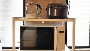 Una cocina con microondas, cocedor de arroz y hervidor sobre una repisa de madera.