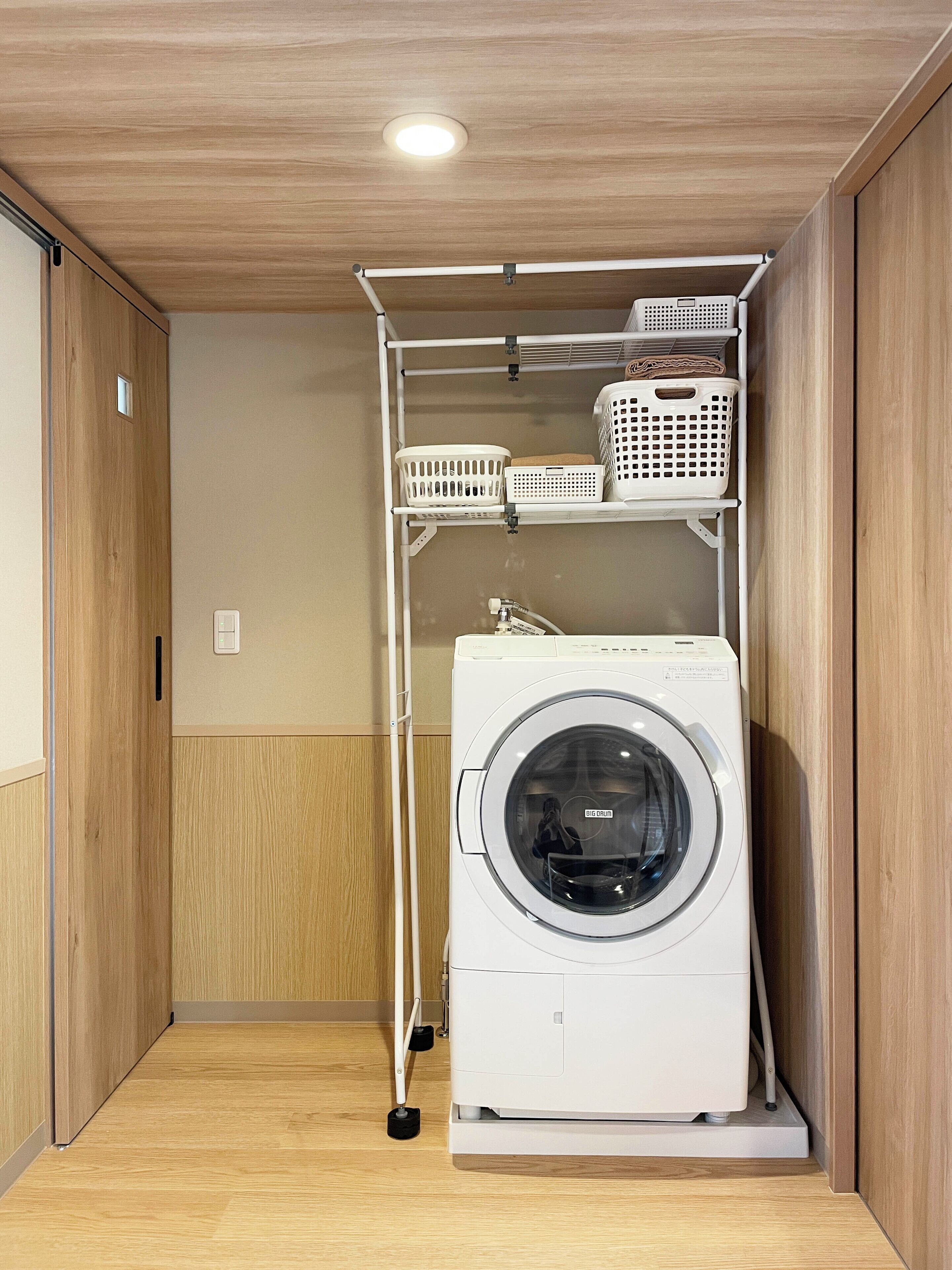 A laundry room with a washing machine, shelves with baskets, and a wooden floor.