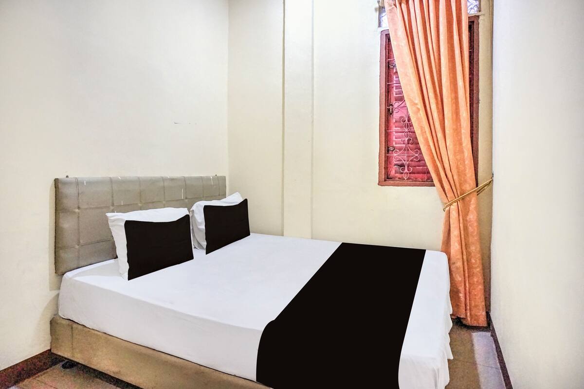 A bed with a headboard, two pillows, a white bedspread, and a black accent.