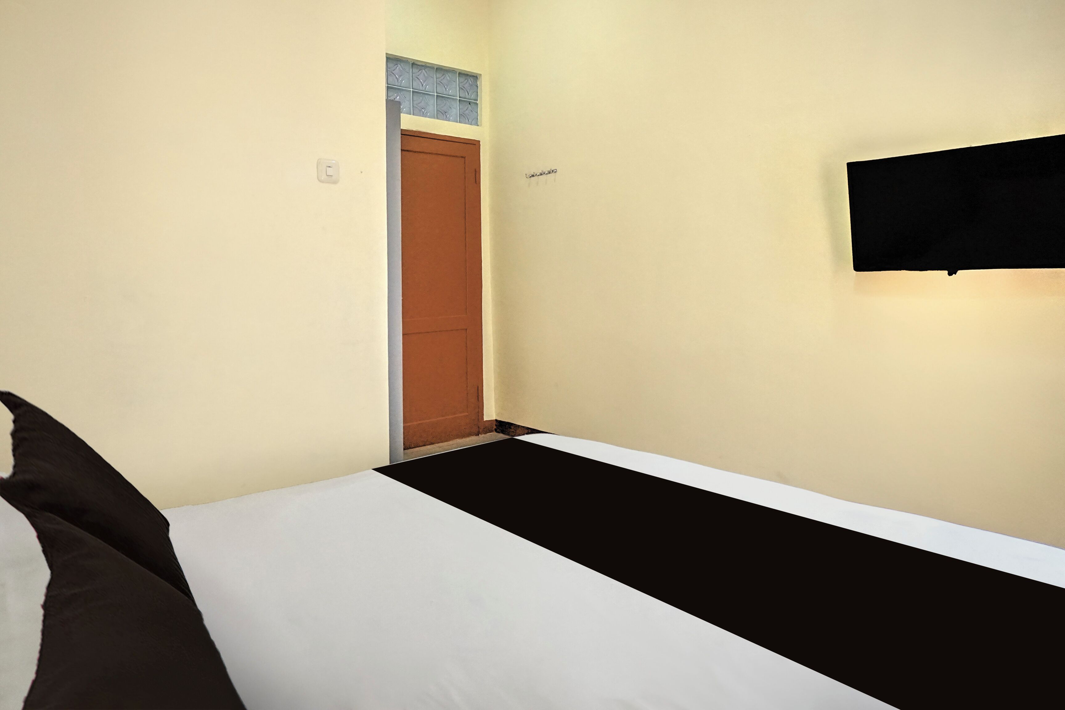 A small, simple room with a bed, a wall-mounted TV, and a door.