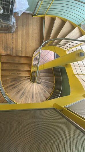 A spiral staircase with a yellow handrail and wooden steps.