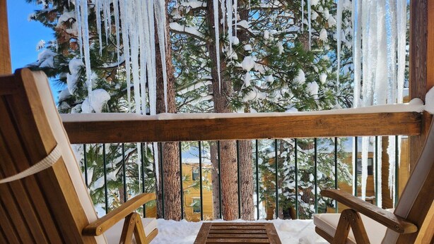 Una terraza de madera con dos sillas y una mesa pequeña, rodeada de nieve y estalactitas.