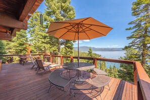 Una terraza de madera con mobiliario exterior, incluyendo una mesa y sillas, y un paraguas grande.