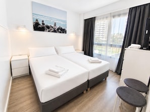 A hotel room with two beds, a desk, and a chair.