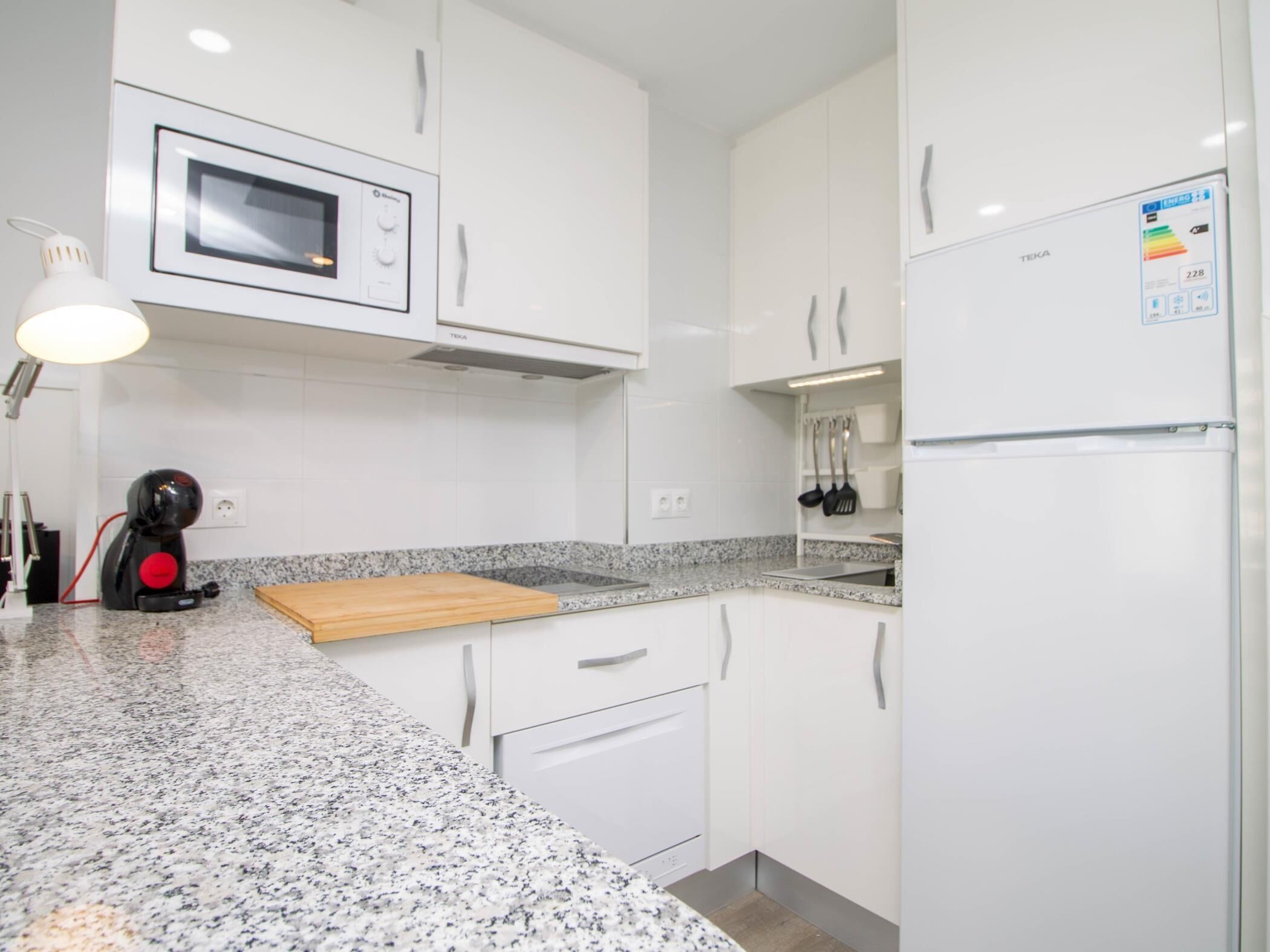 Una cucina moderna con mobili bianchi, un piano di lavoro in granito, un forno a microonde, una macchina da caffè e un frigorifero.