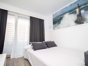 Una habitación de hotel con cama, un cuadro de un faro y vistas de la ciudad a través de la ventana.