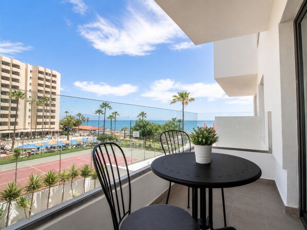 Ein Balkon mit Blick auf einen Pool, Palmen und ein Gebäude gegenüber dem Wasser.