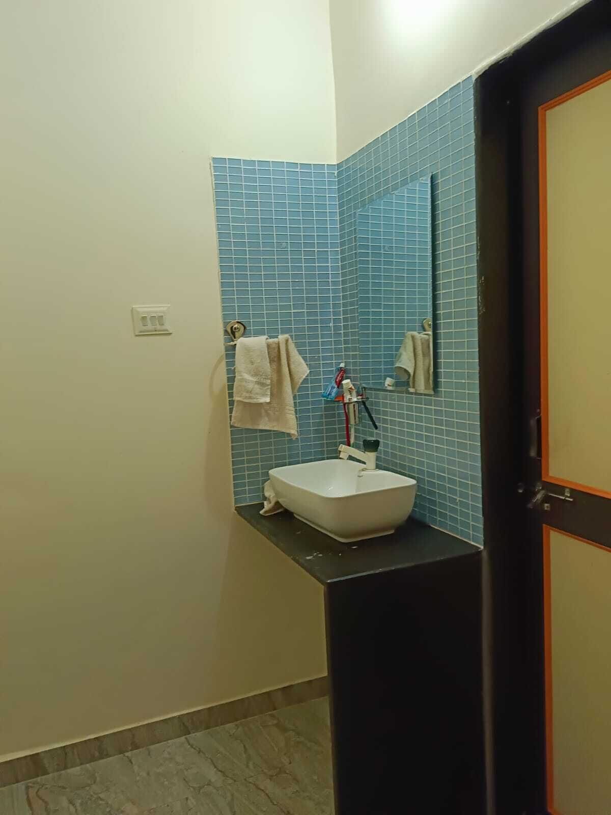 Ein Badezimmer mit einem weißen Waschbecken, blauen Fliesen an der Wand, einem Spiegel und einem Handtuch, das an der Wand hängt.