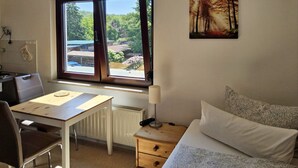 Un dormitorio con cama, escritorio, silla, lámpara y ventana con vistas a zonas verdes.