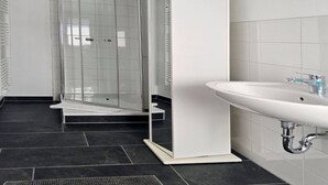 Un baño moderno con ducha de vidrio, lavamanos pedestal blanco y piso de baldosas oscuras.