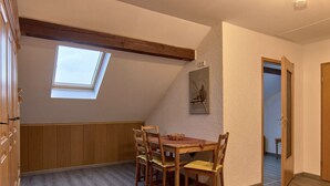 Un coin repas avec une table et des chaises en bois, une lucarne et une porte donnant sur une autre pièce.