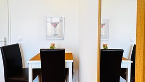 Een eethoek met een witte tafel en zwarte stoelen, een lijst met een afbeelding aan de muur en een houten deurkozijn.