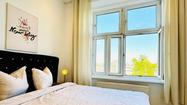 Een slaapkamer met een bed, een raam met gordijnen, een radiator en een wand met een ingelijst kunstwerk.