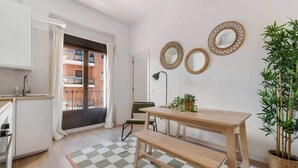 A modern kitchen with a checkered floor, a wooden dining table with benches, and a balcony with a view of a brick building.