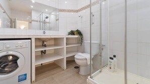 A modern bathroom with a washing machine, toilet, and glass-enclosed shower.
