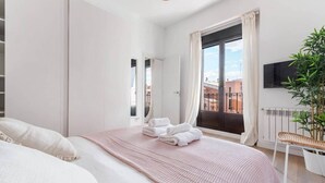 A bedroom with a bed, a window with curtains, a plant, and a TV on the wall.