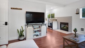 A modern living room with a flat-screen TV, a fireplace, and a kitchen in the background.