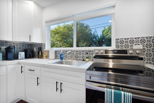 Una cocina con armarios blancos, un horno de acero inoxidable y una ventana con vistas a árboles.