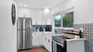 A compact kitchen with white cabinets, a stainless steel refrigerator, a built-in oven, and a window providing natural light.