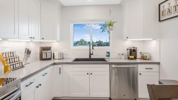 A modern kitchen with white cabinets, a stainless steel dishwasher, and a window providing a view of the outdoors. - Pet-Friendly, Stylish Home w/ Backyard Oasis (Santa Maria)