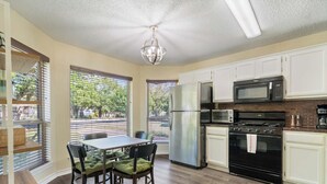 Una cocina con armarios blancos, un refrigerador de acero inoxidable, un microondas, una estufa y un comedor con mesa y sillas.