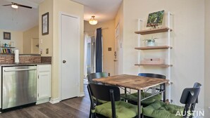 Una cocina compacta con lavavajillas, una mesa de comedor con sillas y una estantería con objetos decorativos.