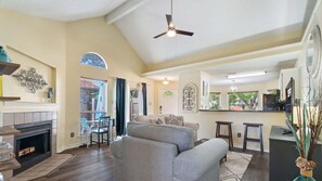 A spacious living room with a fireplace, a sofa, a dining area, and a kitchen with a TV.