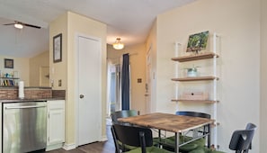 A compact kitchen with a dishwasher, a dining table with chairs, and a shelving unit with decorative items. - Cozy North Austin Home | Pet-Friendly | Grill | Close to Shopping & Trails (Austin)