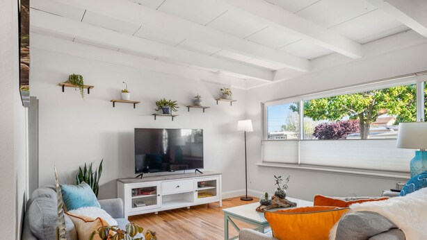 A modern living room with a flat-screen TV, white furniture, and multiple potted plants on shelves.