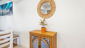 A white wall with a round mirror, a wooden cabinet with decorative doors, and a potted plant.