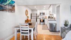A modern kitchen with white cabinets, stainless steel appliances, and a dining area with a wooden table and white chairs.