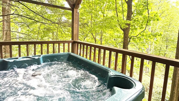 Ein Whirlpool auf einer Holzterrasse mit Blick auf grüne Bäume.