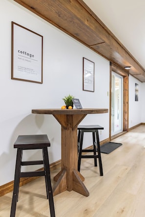 Ein Flur mit einem Holztisch und zwei Hocker, gerahmten Bildern an der Wand und einer Tür am Ende.