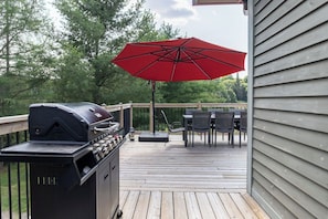 Une terrasse en bois avec un barbecue, du mobilier d’extérieur et un parasol rouge.