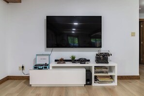Ett modernt vardagsrum med en platt-TV som är monterad på väggen, en vit möbel för underhållningsutrustning med en skivspelare, en gammal skrivmaskin och en bokhylla.