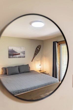 Um quarto com cama, mesa de cabeceira, luminária, quadro e janela com cortinas.