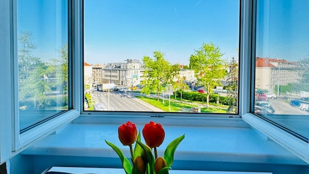 A window with a view of a cityscape, a window sill, and a vase with flowers. - Convenient Room in Shared Apt | Walk to Kaufpark (Vienna)