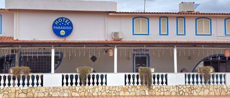 Hotel llamado 'HOTEL PARADISO' con zona de recepción, pared de piedra y plantas decorativas.