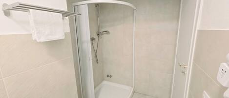 Ducha en esquina con mampara de vidrio, toallero y retrete.