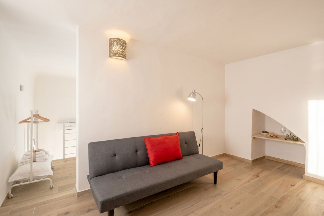 A modern living room with a grey sofa, a red pillow, a floor lamp, and a small shelf with snacks.