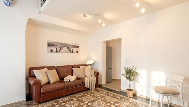 A living room with a patterned floor, a brown leather sofa, a white chair, a potted plant, and a painting on the wall. - Gabbiano 2 - Sea Loft  (Bari)