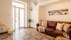 A living room with a brown leather sofa, a patterned floor, a potted plant, and a painting on the wall. - Gabbiano 2 - Sea Loft  (Bari)